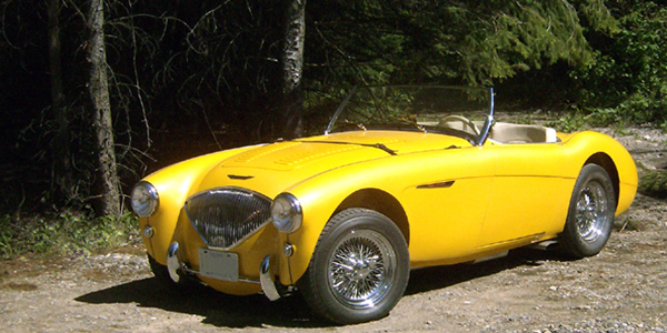 Yellow Austin Healey infront of trees